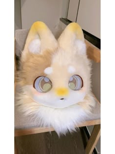 a stuffed animal with big eyes sitting on top of a wooden chair next to a wall