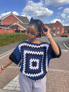 a woman standing on the side of a road wearing a blue and white crocheted sweater