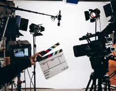 a person holding a camera in front of a bunch of lights and cameras on a tripod