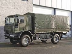 an army green truck parked in front of a building