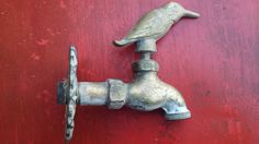 an old faucet with a bird on it's head is attached to a red wall