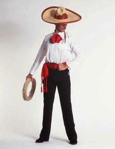 a man in a sombrero and tie holding a hat on his head while standing against a white background