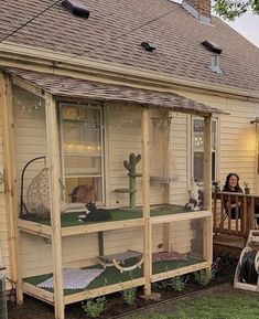 a woman sitting on a porch next to a house with a cat in the window