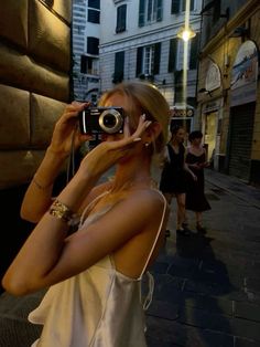 a woman taking a photo with her camera on the street in front of some buildings