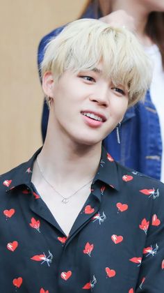 a man with blonde hair wearing a black shirt and red hearts on it's chest