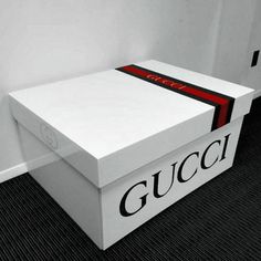 a white gucci box with a red and green stripe on the lid sitting in a corner