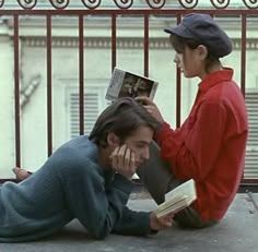 two people sitting on the ground with books in their hands and one person holding an open book