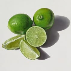 limes cut in half and whole on a white surface with shadow from the top