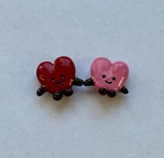two red and pink heart shaped buttons sitting on top of a white surface with one holding the other's hand