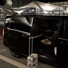 a black van is parked at an airport with its door open and luggage next to it