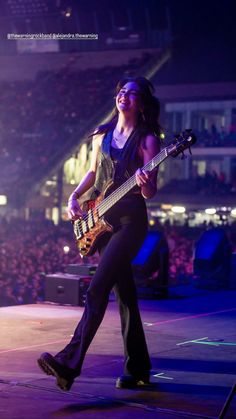 a woman holding a guitar while standing on top of a stage with an audience in the background
