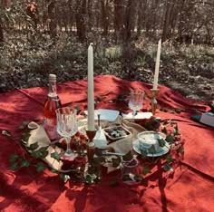 the table is set with candles, plates and glasses for two people to enjoy in the woods