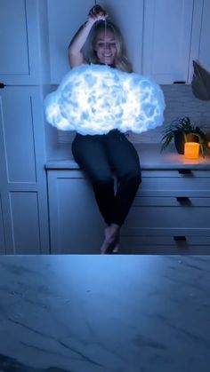 a woman sitting on top of a kitchen counter holding a cloud like object above her head