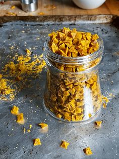 a glass jar filled with yellow food sitting on top of a metal counter next to a wooden cutting board