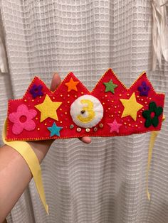 a hand holding up a red crown with stars on it and a number one in the middle