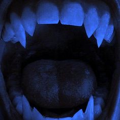 the mouth of an animal with sharp teeth is lit up in blue light from below
