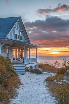 a house sitting on top of a lush green hillside next to the ocean at sunset