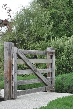 an old wooden gate is open in front of some bushes