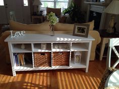 a white table with baskets and flowers on it in a living room next to a couch