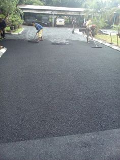 two men are working on the asphalt in front of a building with several other people nearby
