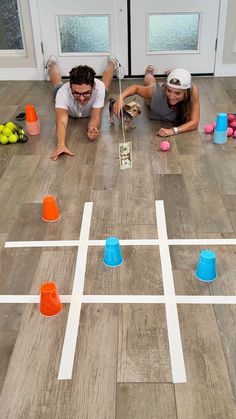 two people laying on the floor playing with plastic cups and an interactive game for kids