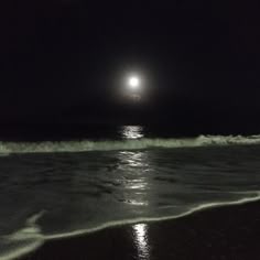 the moon is shining over the water at night on the beach with waves coming in