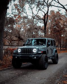 a gray jeep parked on the side of a road next to a tree filled forest