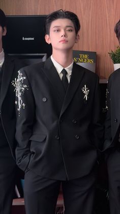 two young men in suits standing next to each other near a book shelf with books on it
