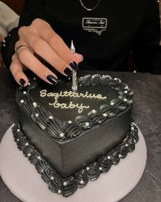 a woman is cutting into a heart shaped cake with black frosting and pearls on it