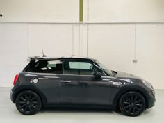 a grey mini hatchback parked in a garage with white walls and black rims