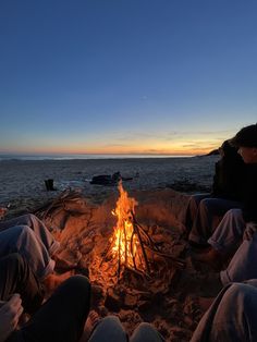 three people sitting around a campfire on the beach