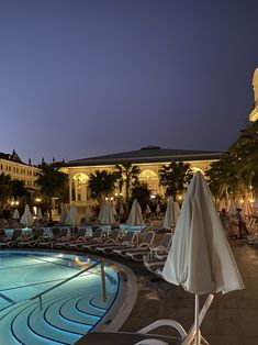 an outdoor swimming pool at night with lounge chairs and umbrellas in the foreground
