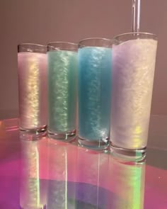 three glasses filled with liquid sitting on top of a pink and blue tablecloth next to each other