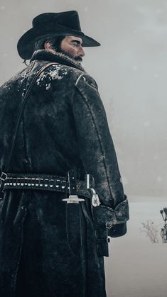 a man in a black coat and hat standing on snow covered ground with his back to the camera