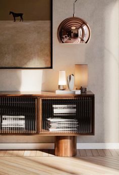 a wooden table topped with lots of books next to a wall mounted art piece and lamp