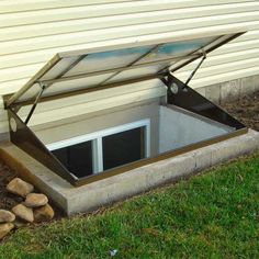 an open skylight on the side of a house next to some rocks and grass