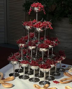 a table topped with lots of red cherries next to silver cups and saucers