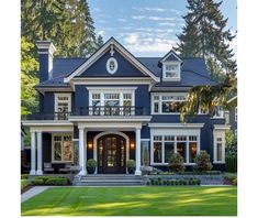 a large blue house with white trim on the front and side windows, surrounded by lush green trees