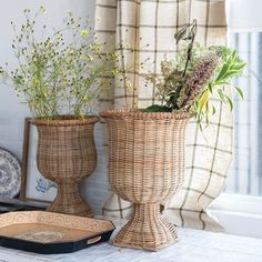 two wicker vases with plants in them sitting on a table next to a window