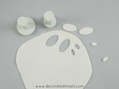 a white plastic ghost face with holes in the middle and two other pieces next to it on a gray surface
