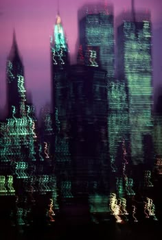 the city skyline is lit up in green and purple colors as seen through a window