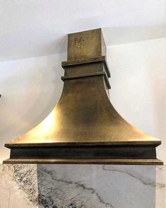 a large gold stove hood mounted on the side of a wall with marble counter tops