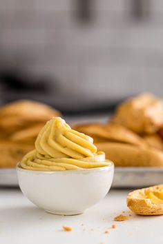 a white bowl filled with yellow frosting next to some bread rolls on a plate