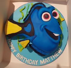 a blue and yellow birthday cake with an image of a fish on the side, in a box