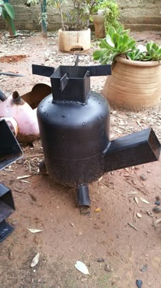 a black stove sitting on top of a dirt ground next to a potted plant