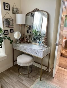 a dressing table with a mirror, stool and plant on it next to a window
