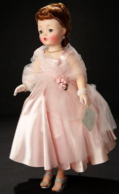 an old doll wearing a pink dress and matching shoes is standing on a black surface