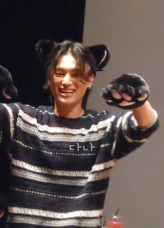 a man in a black and white striped shirt holding two cats on his shoulders with both hands
