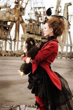 a woman in a red jacket and black dress holding two stuffed animals