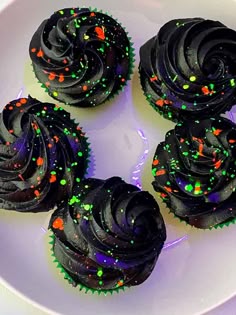 four cupcakes with black frosting and sprinkles on a plate